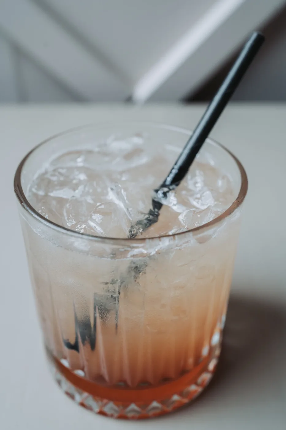 A tumbler of an iced red and clear layered drink with a black straw