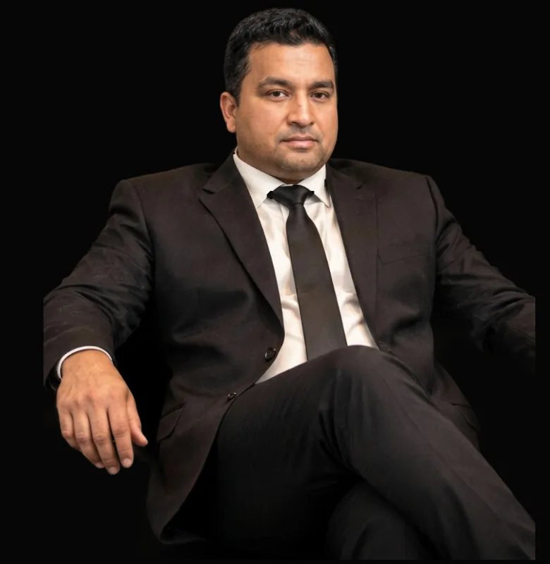 Kawaljit, restaurant manager at Anaya, seated in a dark suit and tie against a black background
