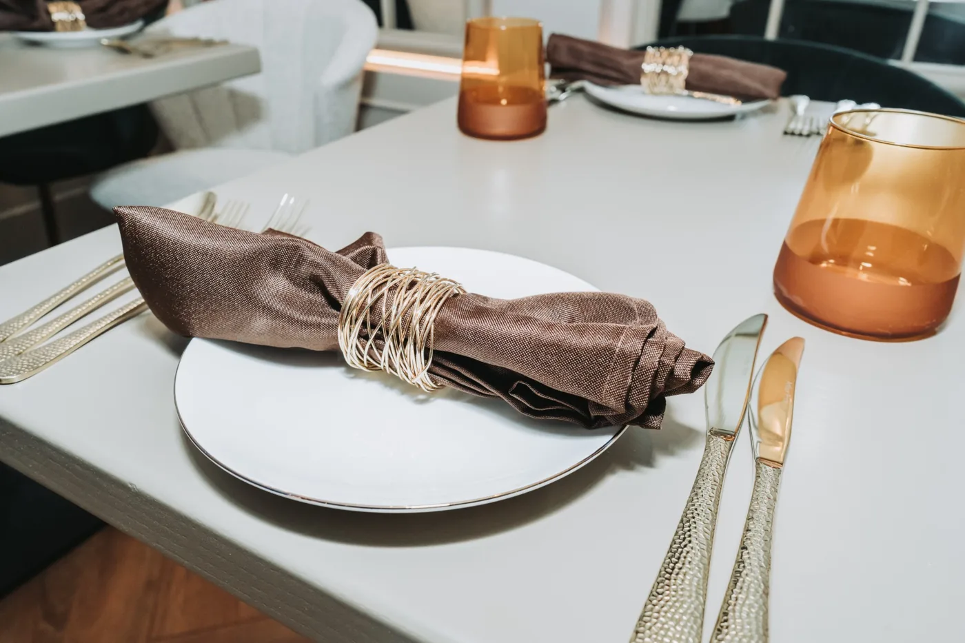 A table laid at Anaya with a white plate, a brown napkin tied with twine, gold cutlery and an amber glass