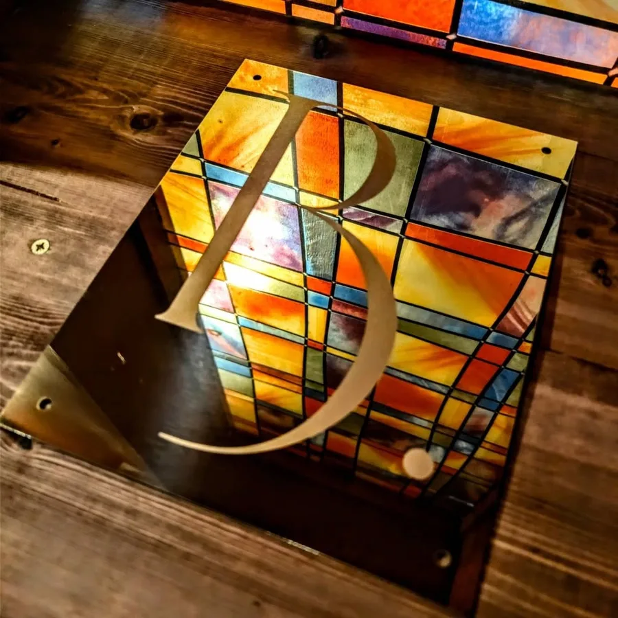 A brass letter B fixed over a coloured stained-glass panel, the sign for Brut and Barrel
