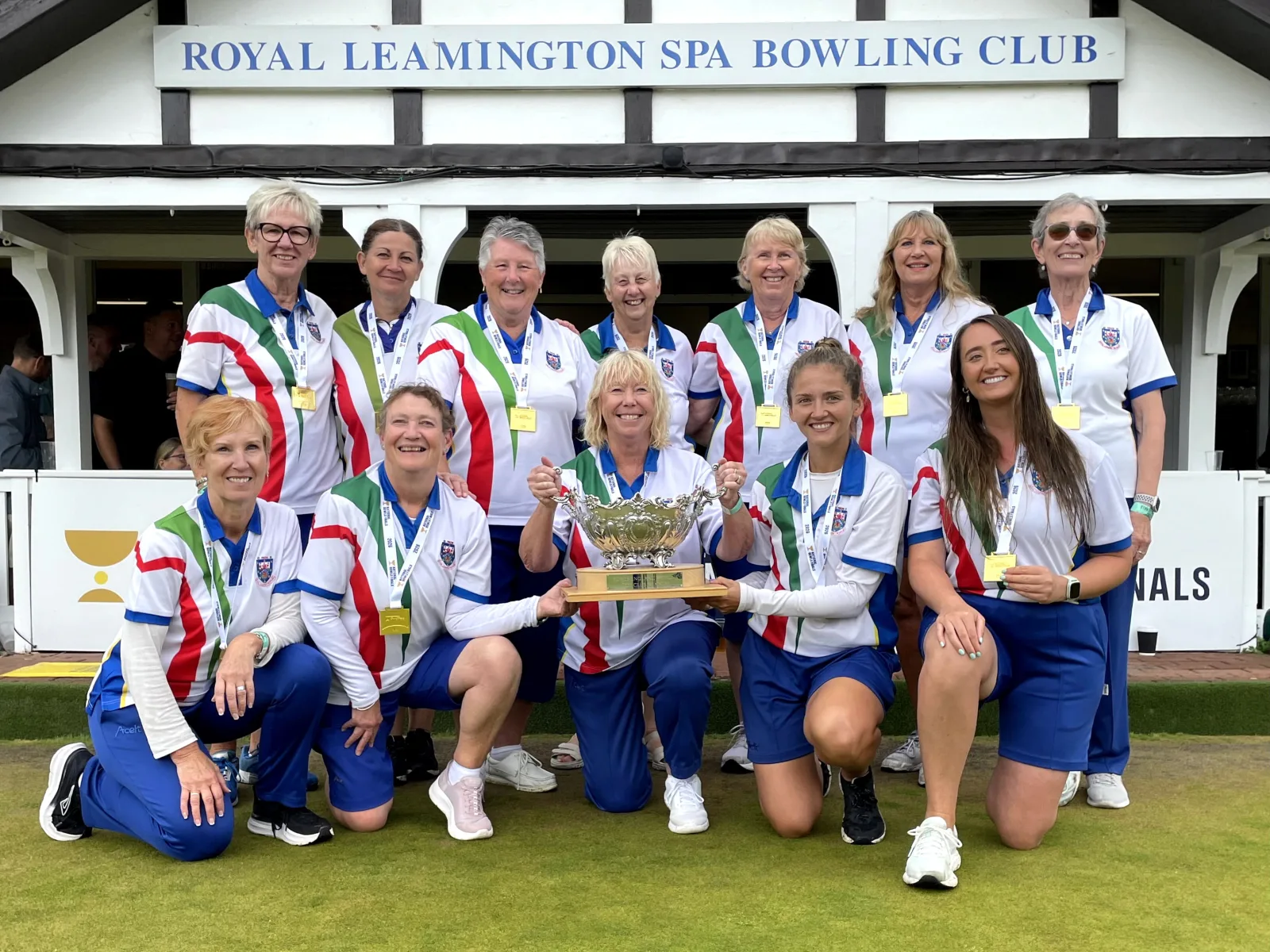 The Royal Leamington Spa women's Top Club team with the trophy outside the club pavilion at Victoria Park after the 2026 final.