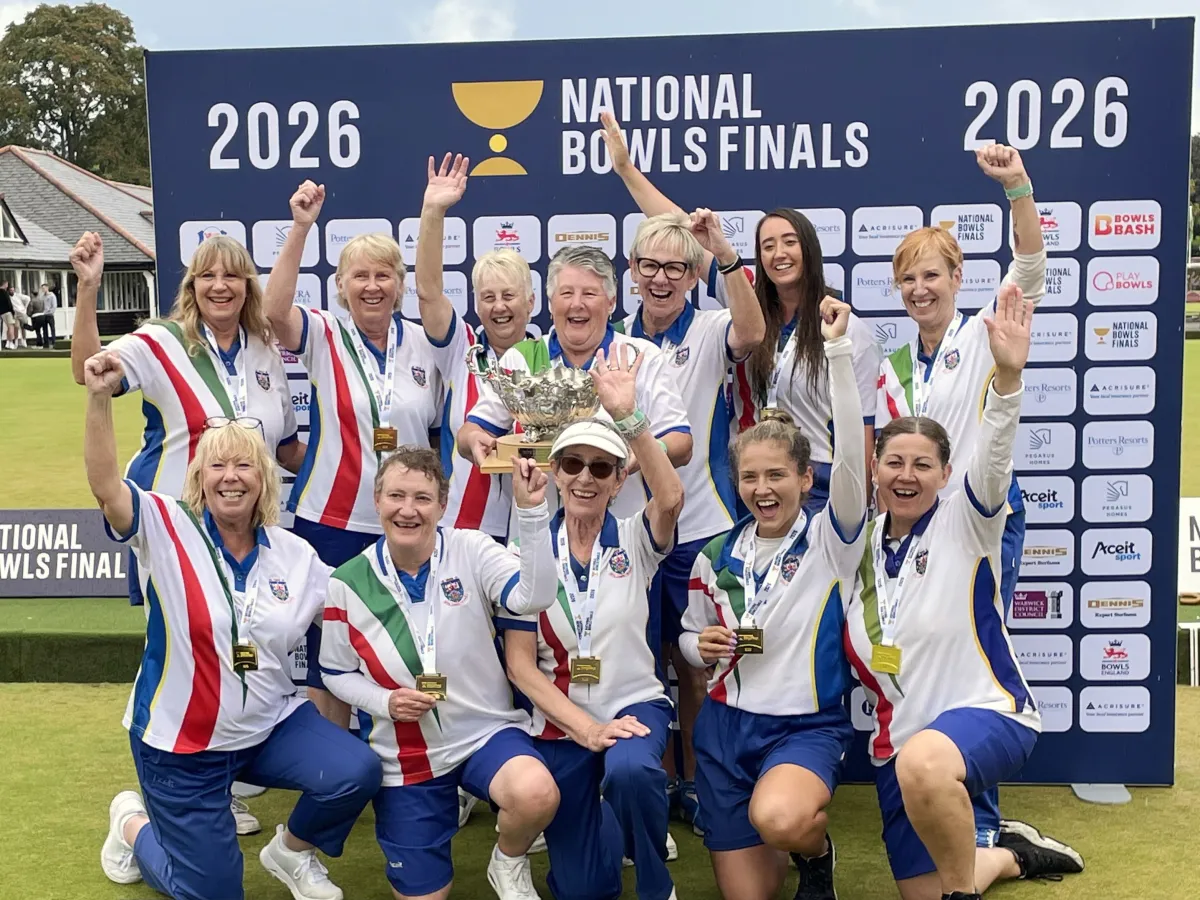 The Royal Leamington Spa women's team celebrating with the Top Club trophy in front of the 2026 National Bowls Finals backdrop at Victoria Park.
