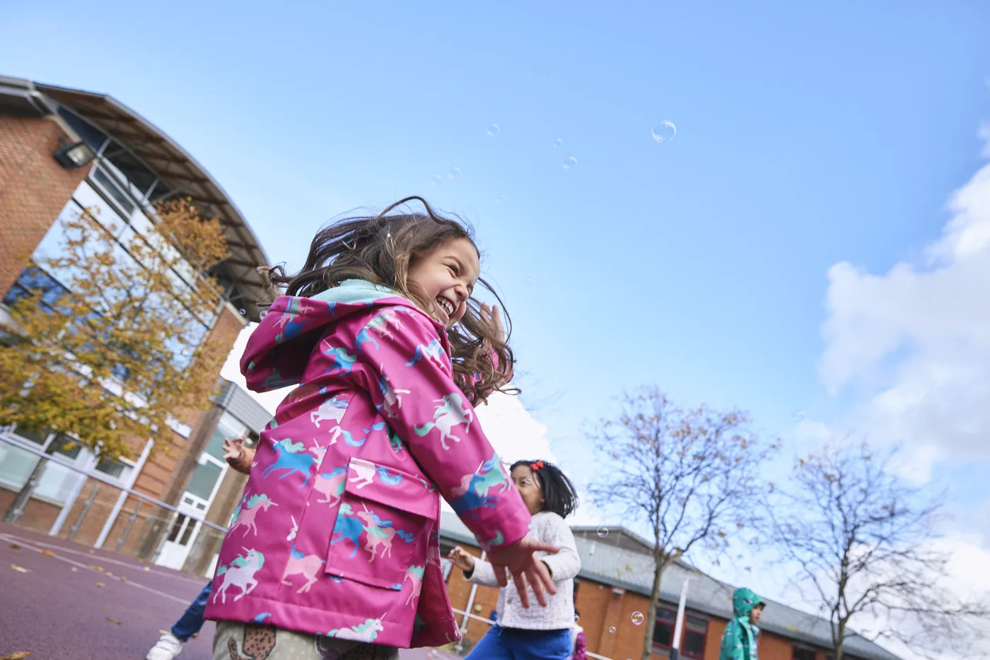A girl in a pink coat running across a school playground under a blue sky