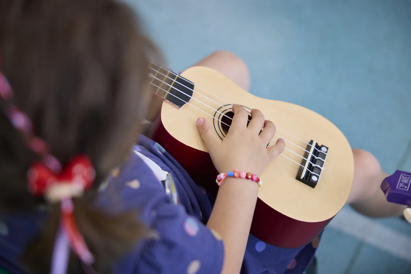 A child's hand on the strings of a small wooden ukulele