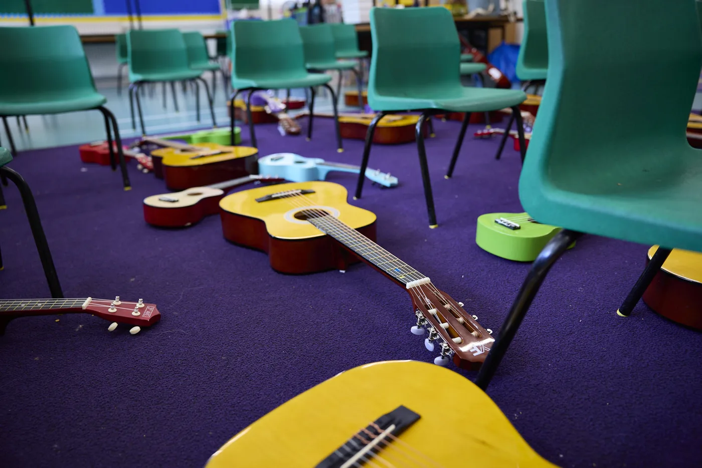 Guitars and ukuleles lying on a purple carpet between green classroom chairs