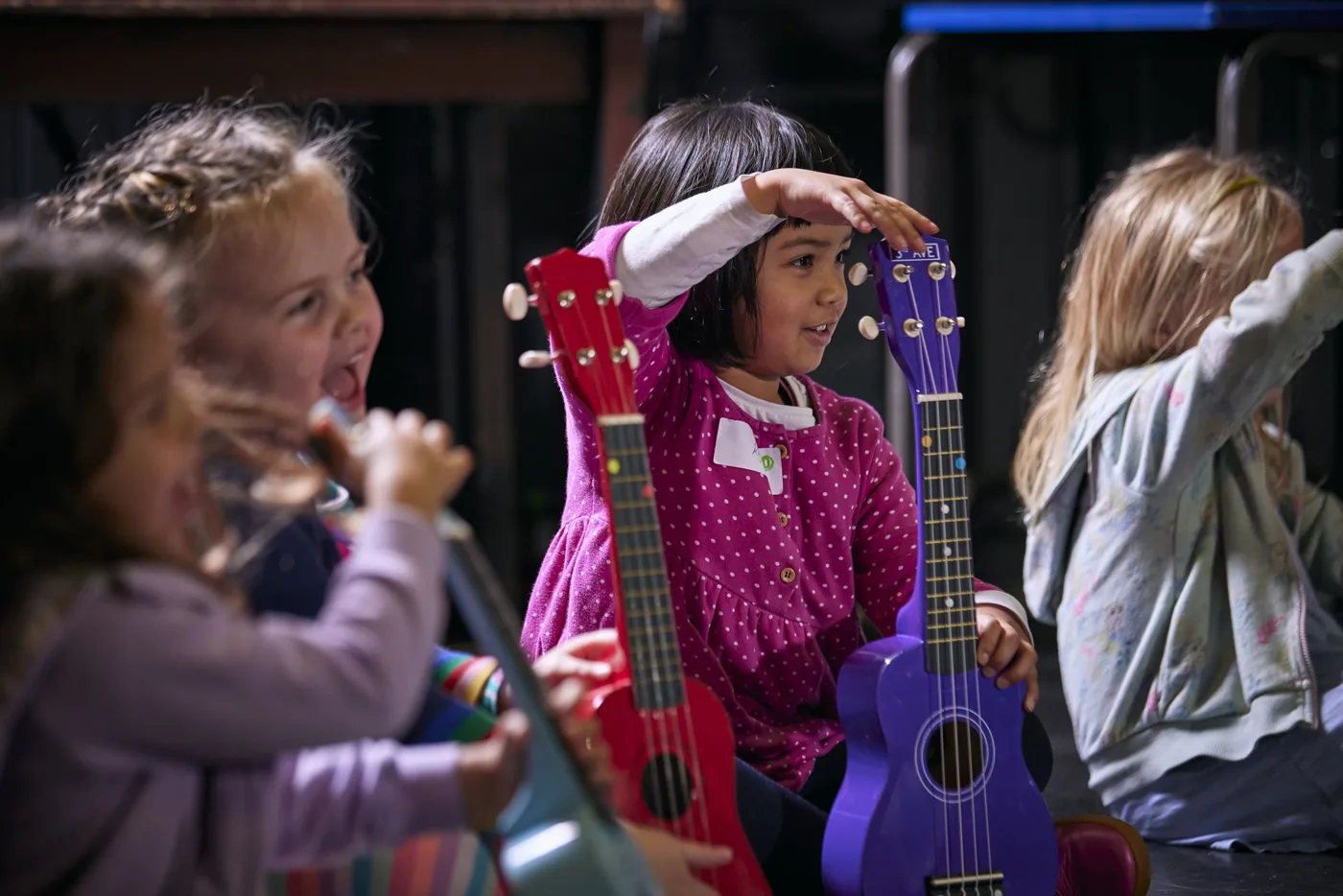 Young children laughing and holding red and purple ukuleles