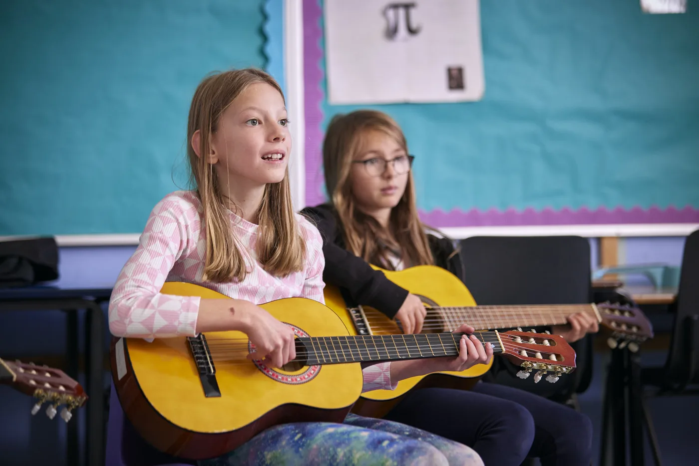 Two girls playing acoustic guitars in a classroom